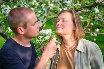 Obraz premium Portrait of a smiling adult woman and a young man walking in a spring apple orchard