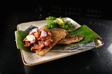 grilled grouper fish fillet with spicy onion sambal chilli sauce on banana leaf in dark background asian halal seafood menu