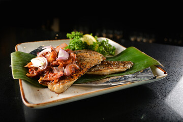 grilled grouper fish fillet with spicy onion sambal chilli sauce on banana leaf in dark background asian halal seafood menu