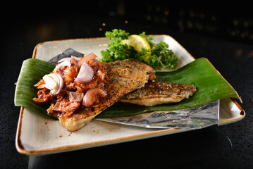 grilled grouper fish fillet with spicy onion sambal chilli sauce on banana leaf in dark background asian halal seafood menu