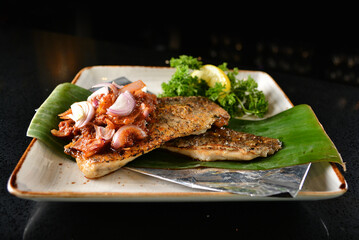 grilled grouper fish fillet with spicy onion sambal chilli sauce on banana leaf in dark background asian halal seafood menu