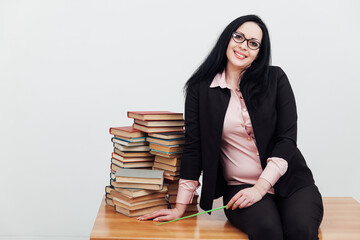 beautiful female teacher in class at a table with stacks of educational books