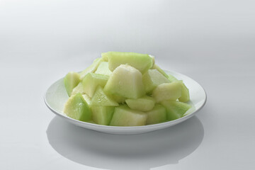 Small pieces of melon in a white plate on white background.