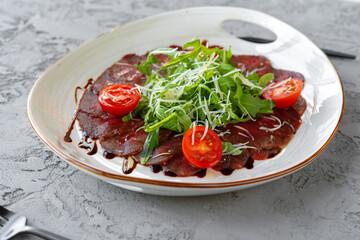 Beef carpaccio with arugula and parmesan on gray surface