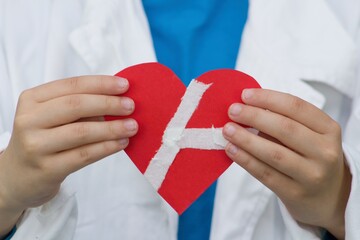 A doctor holds red paper heart stuck with plaster.Concept on the theme of heart disease, surgery...