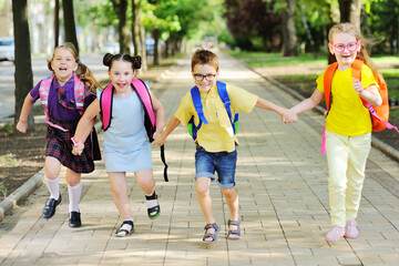 Obraz premium a group of school children in colored clothes with school bags and backpacks run to school smiling. School year, back to school, knowledge day.