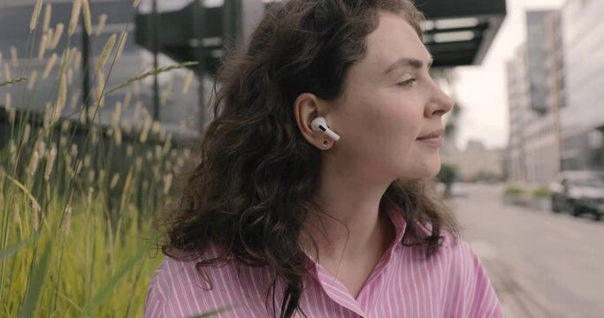 Attractive young woman listening the music in wireless in-ear headphones use smartphone. Apple AirPods Pro. Walk in the city, sit and look around. Smile portrait.