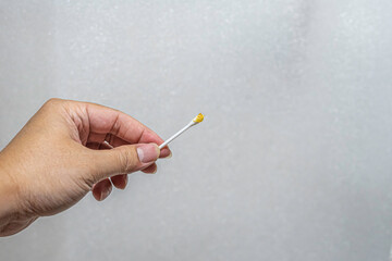 Close up of hand holding on cotton bud and earwax.