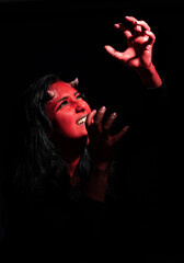 Screaming  woman with long black hair and with face paint for halloween, demon woman with red face and small horns on black background. Halloween concept. Halloween Makeup