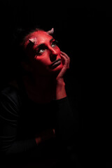 Portrait of sexy woman with long black hair and with face paint for halloween, demon woman with red face and small horns on black background. Halloween concept. Halloween Makeup