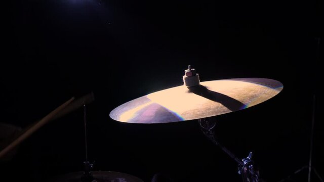 cymbal spins and reflects the bright spotlights. white musician passionately beats the drum on a dark background