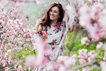 Beautiful woman in a dress with flowers walks through the flowering garden in spring