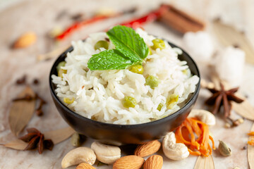 Close-up of Indian Basmati steamed Rice or matar (Pea) pulao or Pulav garnished with fresh green mint leaf in a black bowl.