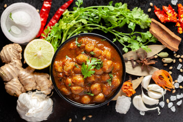 Chickpeas masala (Spicy chola or chhole curry)  garnished with fresh green coriander and ingredients. Served in a black bowl. A Classic Indian typical Panjabi street food.