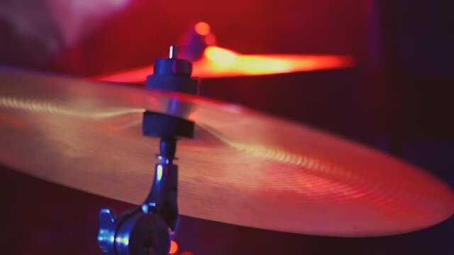 musician holds drumsticks and plays actively on stage. from the impact, the cymbals shake and vibrate. close-up on a background of red and blue rays