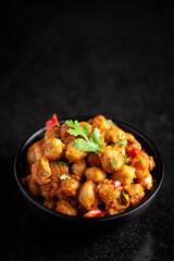 Chickpeas masala (Spicy chola or chhole curry)  garnished with fresh green coriander and ingredients. Served in a black bowl. A Classic Indian typical Panjabi street food.