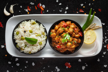 Chickpeas masala (Spicy chola or chhole curry) and Pulav (Rice) garnished with fresh green coriander and ingredients. Served in a black bowl. An Classic Indian typical Panjabi street food
