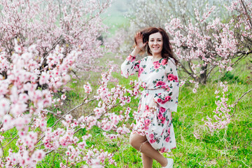 Beautiful brunette woman in a dress with flowers in pink blossoming peach garden spring