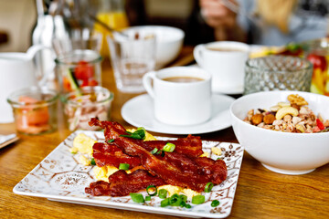Table laid for breakfast outside in summer with various jams, bread, coffee, croissants, eggs, bacon muesli and orange juice