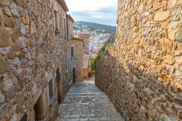 Narrow street with stone walls and floor of an old village in Tossa de Mar.