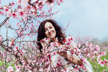 Beautiful brunette woman in a dress with flowers in pink blossoming peach garden spring