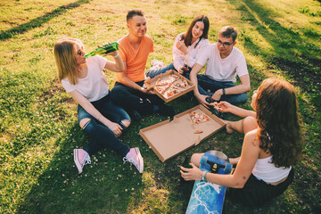 Five young cheerful friends eating pizza outdoors