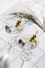 Martini cocktail with olives on the tiled table. An alcoholic classic drink with ice in an elegant glass