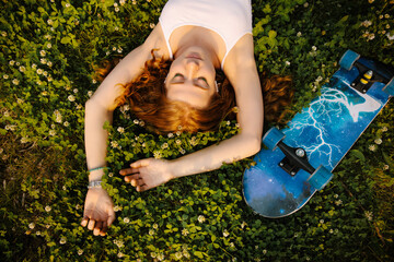 Redhead curly girl skater lies on the grass