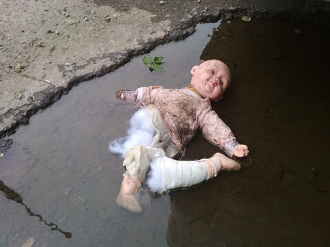 a torn, broken baby doll in a puddle.