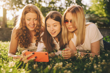 three young girls lie on the grass and look in surprise at the smartphone