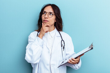 Young doctor mexican woman isolated on blue background looking sideways with doubtful and skeptical expression. - obrazy, fototapety, plakaty