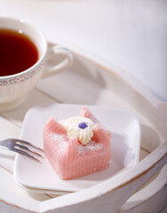 Pink petit four on a white saucer. A cup of tea on a white tray, perfect Sunday breakfast