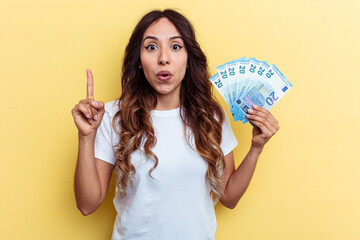 Young mixed race woman holding bills isolated on yellow background having some great idea, concept of creativity.