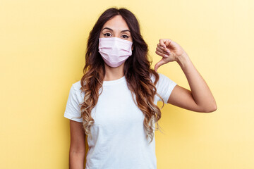 Young mixed race woman wearing a protection for virus isolated on yellow background showing a dislike gesture, thumbs down. Disagreement concept.