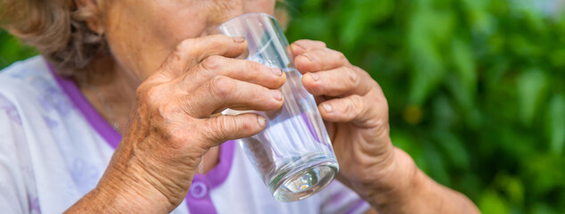 Grandma drinks water from a glass. Selective focus.