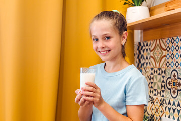 A beautiful little girl drinks a glass of fresh milk in a fashionable modern kitchen, the children's health concept