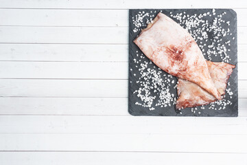 Raw squid carcass with spices and coarse salt on a black slate board. copy space Top view.