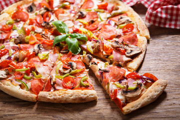 pizza with bacon, salami and vegetables on a wooden table