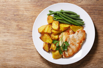 plate of grilled turkey with baked potatoes and green beans on wooden background