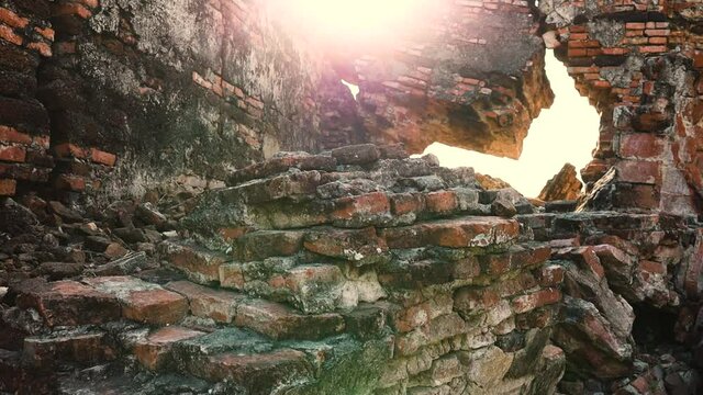 Ruins of old threadbare brick wall. Sun rays shining through cracks in the wall. Camera slowly moving upwards.
