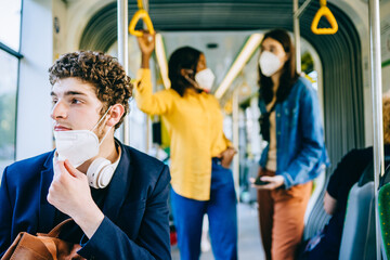 Tired young caucasian man with medical protective medical mask, lowered to the chin. Incorrect wearing of medical masks under quarantine at public transport inside.