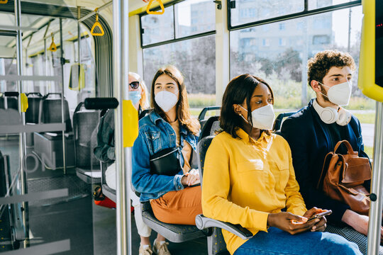 Diverse passengers on Urban Public Transport. African and caucasian people go to work by public transport. Face Mask protection against virus. - Powered by Adobe