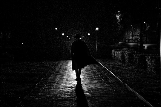 dramatic silhouette of a man in a hat and raincoat walking through the city at night