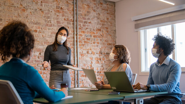 asian business woman leading presentation for teammates with face mask.