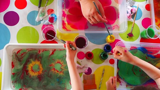 Children draws with paints on water, the Ebru technique, the imprint of the drawing on paper, the childs is engaged in creativity, the teenagers draws an abstract drawing. Top view.