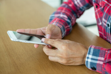 Young man wearing paid shirt hand holding smartphone and checking and replying to emails in the laptop on office desk. He had to work at home due to the coronavirus outbreak.