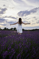 Fototapeta na wymiar Woman in a white dress walks and has fun in the lavender fields. He's on his back with his arms raised