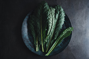 Cavolo nero black curly kale vegetable on black plate - obrazy, fototapety, plakaty