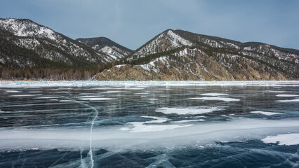 There is some snow on the smooth surface of the frozen lake. There are deep cracks on the ice....