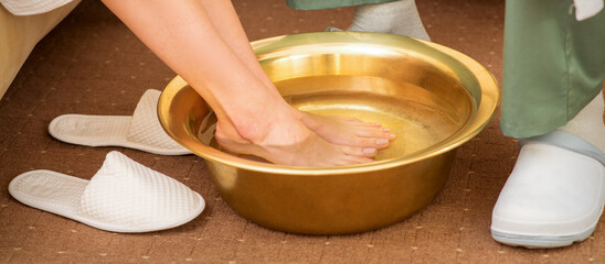 Female feet in a golden bowl with water in spa salon. Spa treatment.